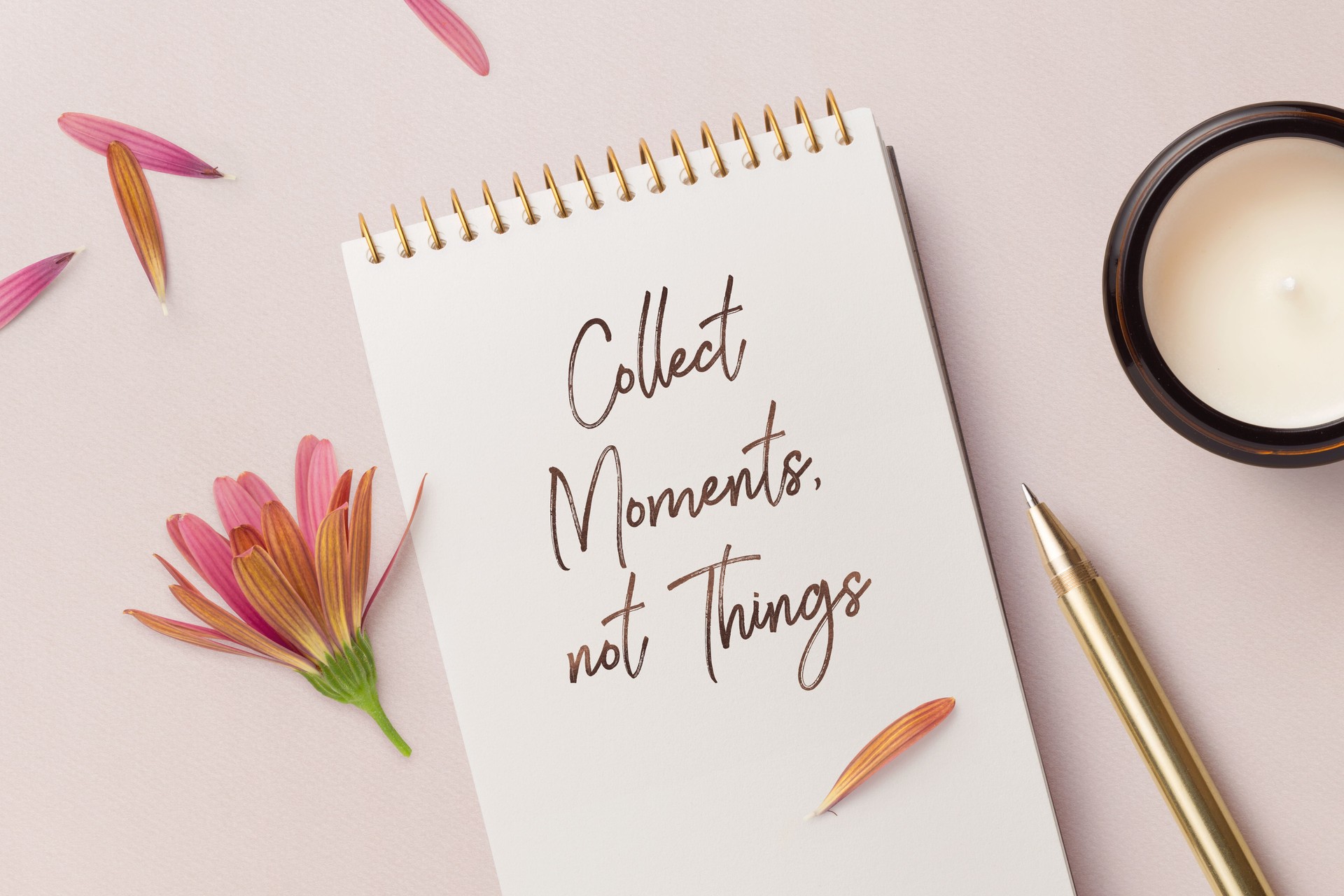 collect moments, not things - motivational / inspirational quote written on a notepad, top view of a minimalist desk with flower, petals golden pen and candles